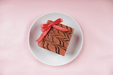 A Cake with A Red Ribbon on A White Plate on A Pink Background