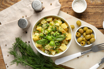 Bowl of tasty potato salad with dill and olives on wooden background