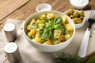 Bowl of tasty potato salad with dill and olives on wooden background