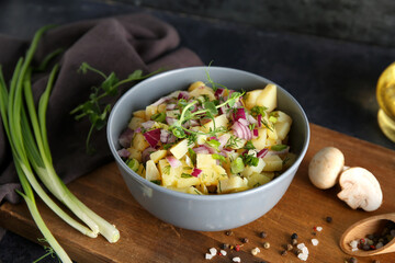 Bowl of tasty potato salad with onion and micro green on black background