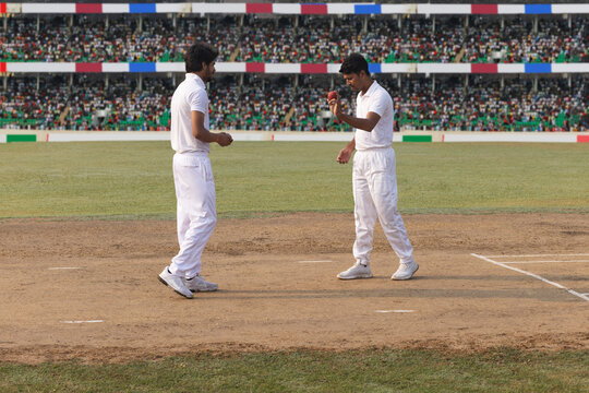 A bowler inspects the pitch while the captain stands behind during a cricket game