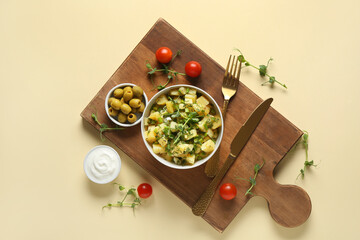 Bowl of tasty potato salad with micro green and olives on yellow background