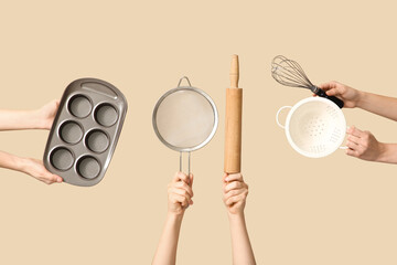 Female hands holding sieve with rolling pin, baking tin and whisk on beige background