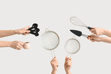 Female hands holding sieves with measuring spoons, cake spatula and whisk on white background
