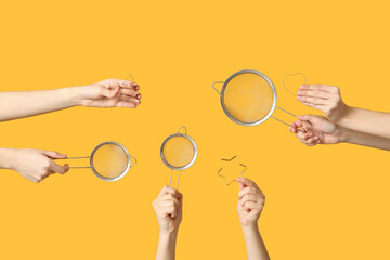 Female hands holding sieves with cookie cutters on yellow background