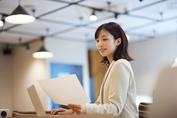 オフィス内でノートパソコンで仕事をする笑顔の日本人ビジネスウーマン