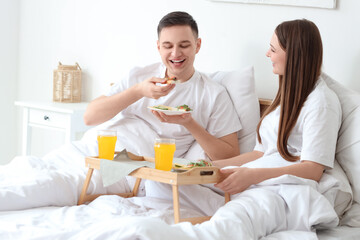 Young couple with sandwiches having breakfast in bedroom