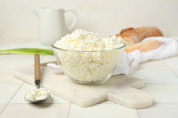 Glass bowl and spoon with fresh cottage cheese on white tile table
