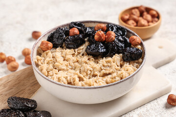 Bowl of tasty oatmeal with prunes and hazelnuts on white grunge background