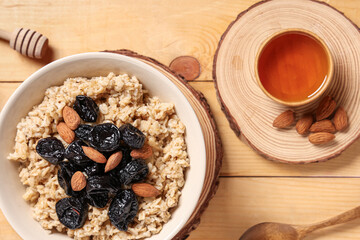Bowl of tasty oatmeal with prunes, almonds and honey on light wooden background