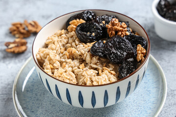 Bowl of tasty oatmeal with prunes and walnuts on grey grunge background