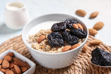 Bowl of tasty oatmeal with prunes, almonds and milk on light background