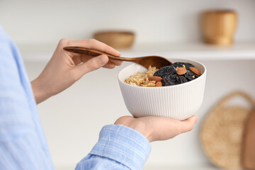 Woman eating tasty oatmeal with prunes and almonds, closeup