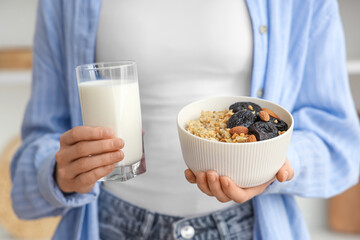 Woman holding bowl of tasty oatmeal with prunes, almonds and glass of milk, closeup
