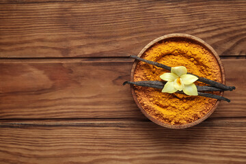 Bowl of turmeric powder, vanilla sticks and flower on wooden background