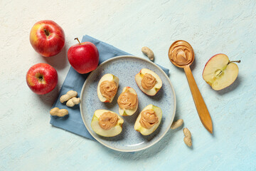 Plate of tasty apple wedges with nut butter and peanuts on light background