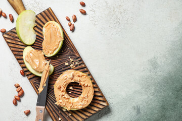 Board with tasty apple wedges, round, nut butter and peanuts on grunge background