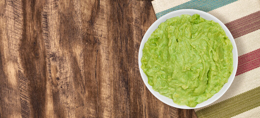 Bowl of fresh guacamole on a wooden table with a striped napkin, top view, ideal for food...
