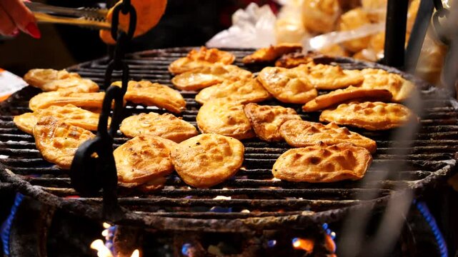 A chef flips Oscypek - Polish regional cheese grilled over fire on a cast-iron grill
