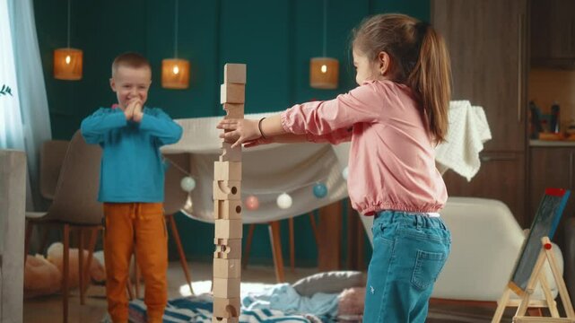 Happy excited little children brother and sister building a big tower of wooden blocks on a floor at home in living room