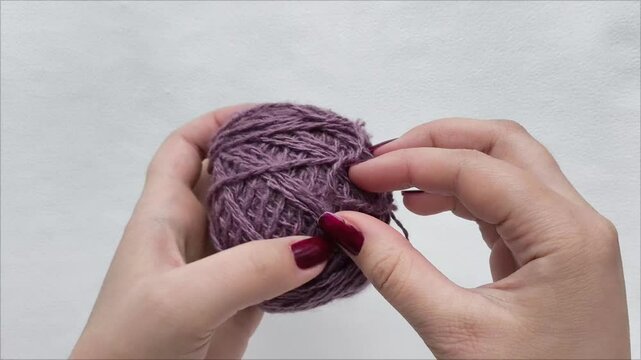 Female hands unwind a ball of purple knitting thread. Wool, yarn in a skein. Knitting lesson.