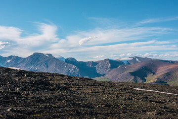 Top view from sunlit stony plain to large multicolor rocky mountains far away in bright sun under...