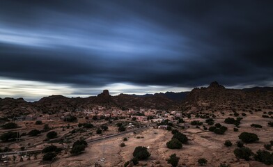 Small village of Aguard Oudad with brightly painted houses in front of the rock Chapeau Napoleon, dramatic clouds, evening, Tafraoute, Anti Atlas, Southern Morocco, Morocco, Africa