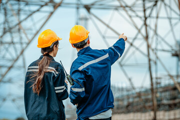 Engineers discussing project details at construction site with power lines and structures in the...