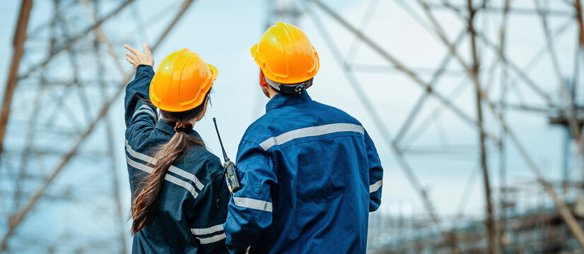 Workers in safety gear discuss project details at an electrical tower construction site during the afternoon