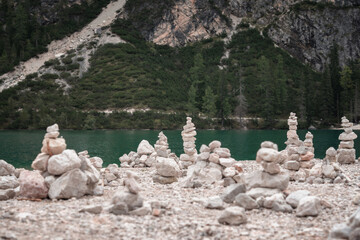A serene landscape featuring multiple balanced stone cairns on a rocky shore, overlooking a beautiful turquoise lake surrounded by lush mountains. The image captures a sense of harmony, nature.