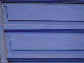 Close-up of a vibrant blue wooden door with textured panels and subtle scratches, creating a rustic and weathered aesthetic.