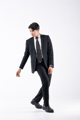 A man in a black suit and tie stands in front of a white background