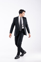 A man in a black suit and tie stands in front of a white background