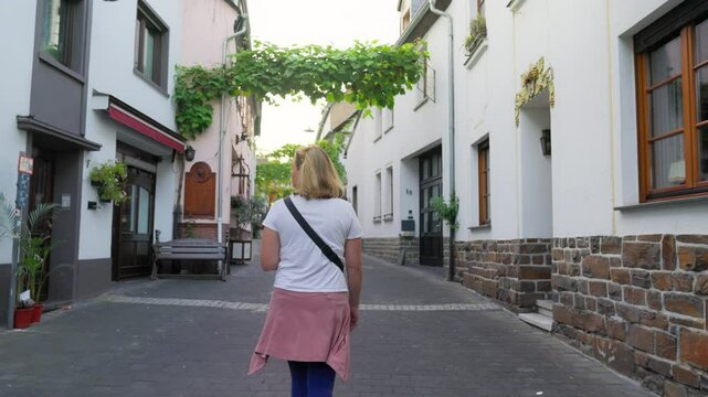Following a tourist walking along the colorful narrow European alleyway featuring wine vines and old white washed buildings, Winningen, Rhine Valley, Germany