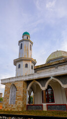A low angle shot that captures the grandeur of the mosque with a minaret and its distinctive green dome in the center against a partly cloudy sky.
