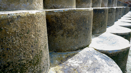 A close-up shot of the weathered concrete sea barrier, its cylindrical shape repeating in receding lines, creating a sense of depth and texture.