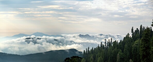 Forest-covered mountains with clouds drifting over them and a serene sky © Shahid Mehmood/imageBROKER