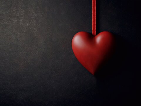 Red heart hanging on satin ribbon on dark background in Valentine's Day style, empty space for text.