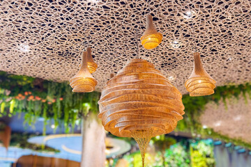 Cozy lightning decor of rattan celling close-up. Decorating hanging lantern lights lamp shade in handcraft wicker made from bamboo. Lampshade in shape of basket from natural material in cafe interior.