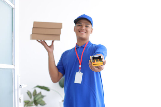 Portrait Of Young Delivery Man Carrying Package Box And Giving EDC Machine To Front For Cashless Payment 