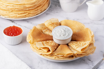 Stack of delicious golden pancakes served with sour cream and red caviar on a marble surface for a delightful breakfast experience