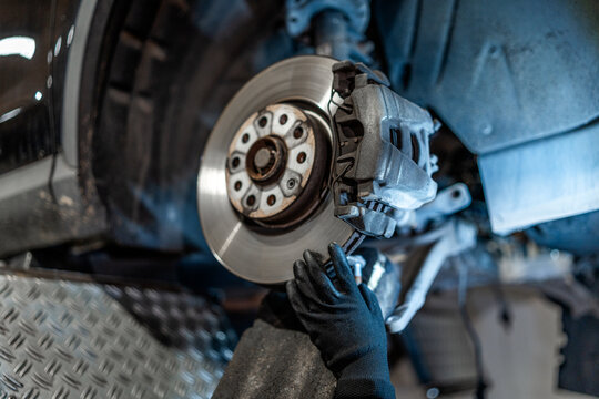 Mechanic inspecting car brake disc and caliper in workshop