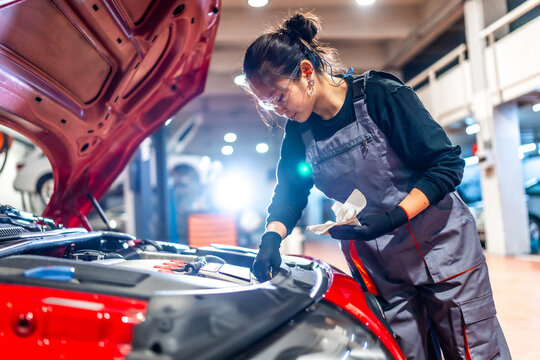 Female mechanic checking oil level in car engine at garage