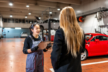Female mechanic delivering repaired car to a customer in a workshop