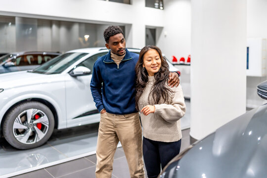 Young multiethnic couple choosing electric car at dealership