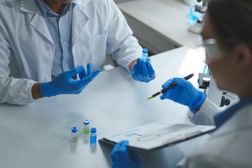 Two scientists wearing lab coats and gloves analyze samples and take notes in a laboratory. They...