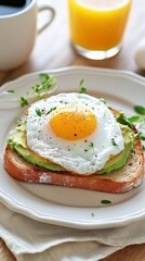 A breakfast toast topped with creamy avocado spread, a sunny-side-up egg and fresh microgreens on rustic bread. With fresh orange juice and a cup of coffee. Suitable for healthy lifestyle or breakfast