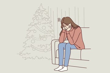 Woman is sitting on sofa near christmas tree and is sad because of loneliness and lack of friends during new year holidays. Christmas melancholy in girl in need of psychological support