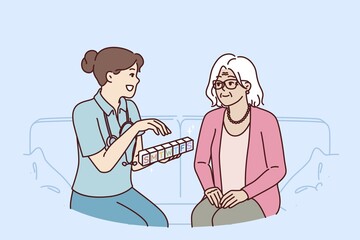 Doctor prescribes medication to elderly female patient and holds pills with smtwtfs letters. Organizer for pills in hands of therapist caring for grandmother suffering from sclerosis