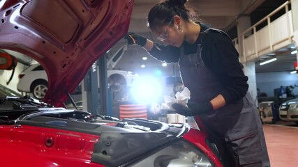 Female mechanic inspecting a car engine in a garage, showcasing skills in automotive maintenance and repair - Powered by Adobe